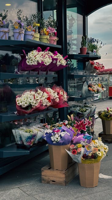 A display of fresh flower arrangements at the flower shop, featuring bouquets of white, pink, and purple blooms wrapped in colorful paper and decorative tissue, arranged on tiered shelves and in bucke